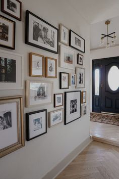 a wall with many framed pictures on it and a door in the backround