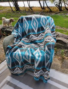 a chair with a blanket on it sitting in front of a lake and a dog