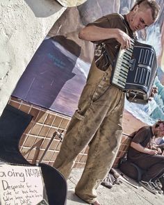 a man is playing an accordion in front of a wall with pictures and writing on it