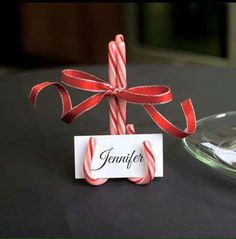 a candy cane with a name tag on it sitting next to a glass bowl and plate