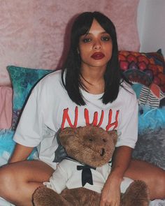 a woman sitting on top of a bed holding a brown teddy bear in her lap