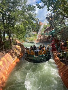 an amusement park ride with people riding on the river and in the water, surrounded by trees