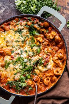 a skillet filled with pasta and sauce on top of a wooden table next to some parsley