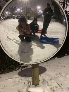 the reflection of two children in a round mirror on a wooden post, with snow and trees behind them