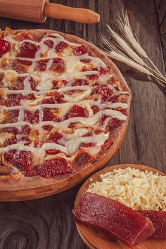 a pizza sitting on top of a wooden cutting board next to cheese and strawberries