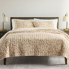 a bed with two lamps on either side of it and a quilted comforter in the middle