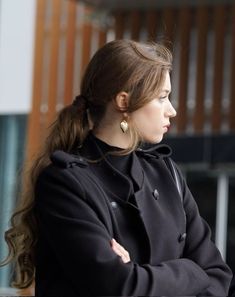 a woman with her arms crossed looking off into the distance while standing in front of a building