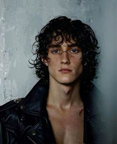 a young man with curly hair wearing a leather jacket