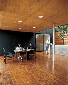 three people sitting at a table in a room with wood flooring and black walls