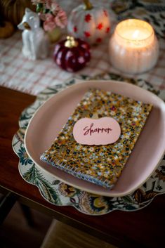 a table topped with a plate covered in a small notebook next to a lit candle