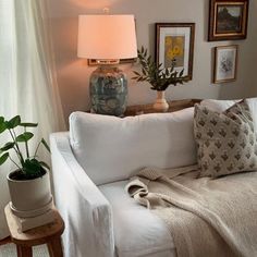 a living room with white couches and pictures on the wall above them, along with potted plants