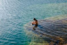 a woman is sitting in the water and looking at her cell phone