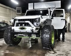 a white jeep parked in a garage next to another car and two men standing near it