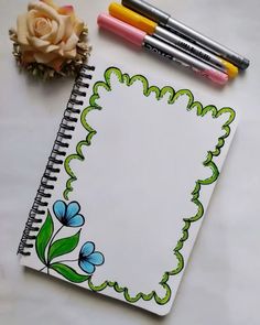 an open notebook with flowers and markers next to it on a white surface, surrounded by two crayons