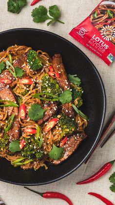 a black bowl filled with noodles, broccoli and other vegetables on top of a table