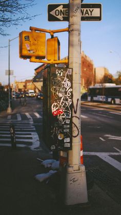 a street sign with graffiti on it next to a traffic light and one way sign