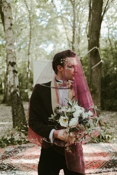 a man in a tuxedo and veil holding a bouquet with flowers on it