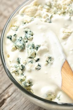 a wooden spoon in a glass bowl filled with cheese and spinach