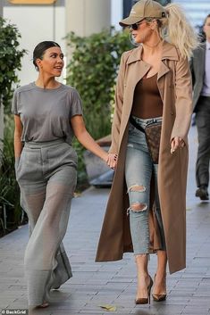 two women are walking down the street holding hands and one is wearing a tan coat