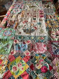 an old quilt is laying on top of a wooden table with chairs in the background