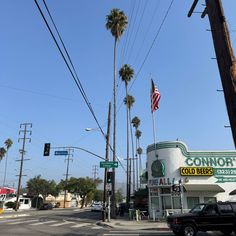 the corner of a street with cars and palm trees in front of a storefront