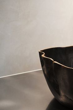 a black bowl sitting on top of a table next to a white wall and floor