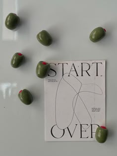 some green olives are laying on top of a book with the words start over it