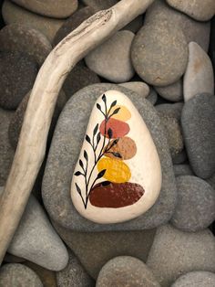 a painted rock sitting on top of a pile of rocks next to a tree branch