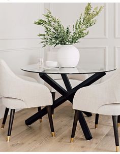 a glass table with two chairs and a vase filled with flowers on top of it