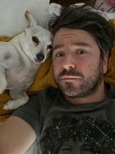 a man laying in bed next to a white dog on top of a yellow blanket