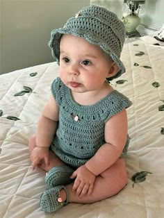 a baby sitting on a bed wearing a crocheted hat and booties with buttons