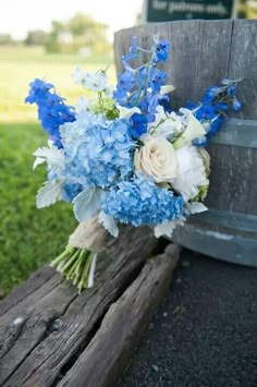 a bouquet of blue and white flowers sitting on a wooden bench next to a barrel