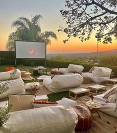 an outdoor movie is set up in the grass with white pillows and chairs around it