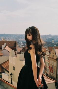 a woman in a black dress standing on top of a building