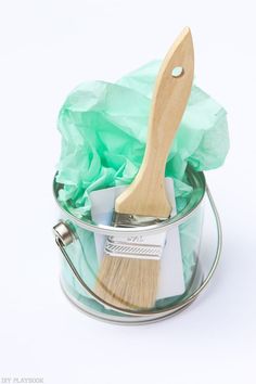 a paint brush in a tin with green tissue paper on the side and a wooden handle