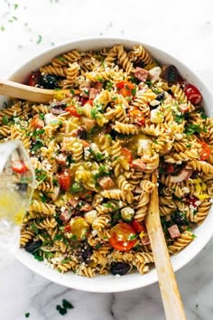 a white bowl filled with pasta salad next to a wooden spoon