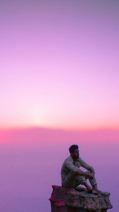 a man sitting on top of a large rock next to the ocean at sunset or dawn