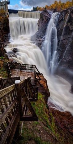 a waterfall that is next to a wooden bridge and some stairs in front of it