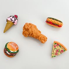 six miniature food items are arranged on a white surface, including an ice cream cone, chicken nugget, and pizza