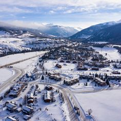 an aerial view of a town surrounded by snow covered mountains and evergreens in the distance