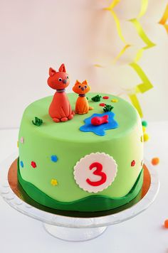 a green cake with two cats on top and the number three is decorated in fondant