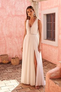 a woman in a long white dress standing on a patio next to a pink building