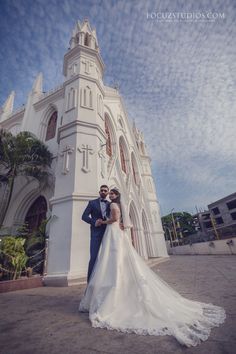 a bride and groom standing in front of a white church with palm trees around them