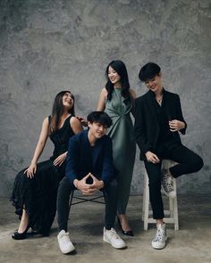 four people sitting on chairs in front of a gray wall and one person standing up