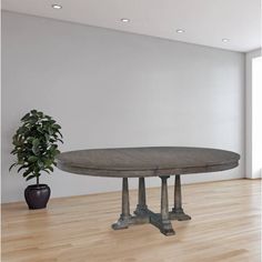 a round wooden table sitting on top of a hard wood floor next to a potted plant