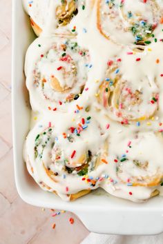 a white dish filled with frosted donuts covered in sprinkles and toppings