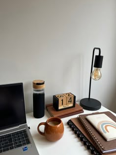 an open laptop computer sitting on top of a desk next to a cup and notebook