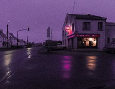 an empty street at night with cars parked on the side and purple sky in the background