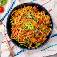 a blue bowl filled with spaghetti and topped with meat, tomatoes, jalapenos and cilantro