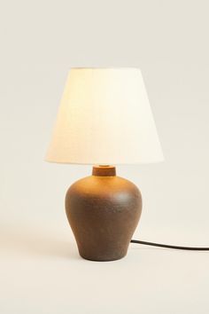 a lamp with a white shade on it sitting next to a black corded light